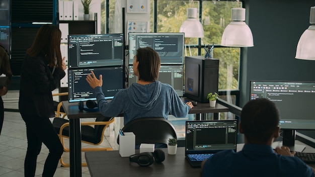 System engineer checking code on multiple monitors and working with app developer colleague in it agency office. Coder analyzing algorithm on screens, developing new user interface.