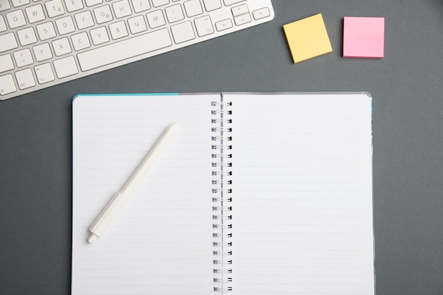 Tastatur over et bord ved siden af en notesbog og kuglepenne med sticky notes computertastatur oven på en