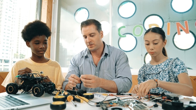 teacher teaching diverse students fixing car model by using wire edification
