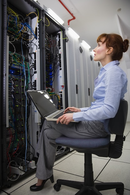 Technician sitting on swivel chair using laptop to diagnose servers