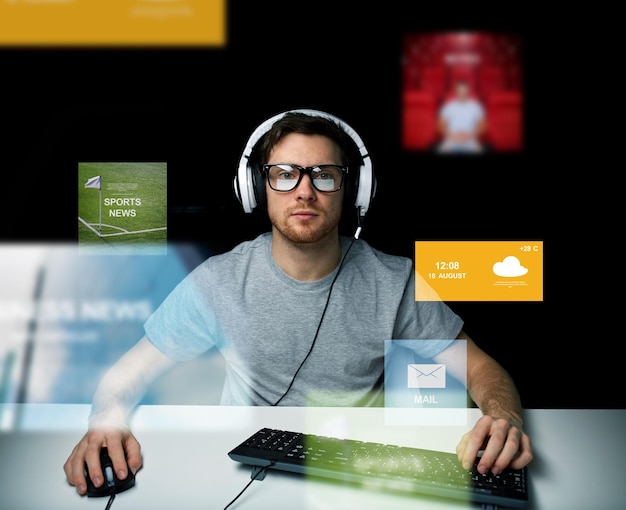 technology, communication, mass media, virtual reality and people concept - young man in headset and eyeglasses with pc computer keyboard over virtual screens