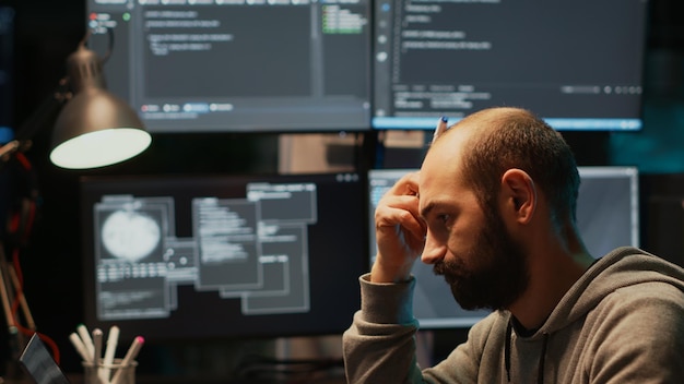 Thoughtful IT engineer brainstorming ideas in office, programming script and source code. Pensive man thinking about coding solution, developing app with html language late at night.