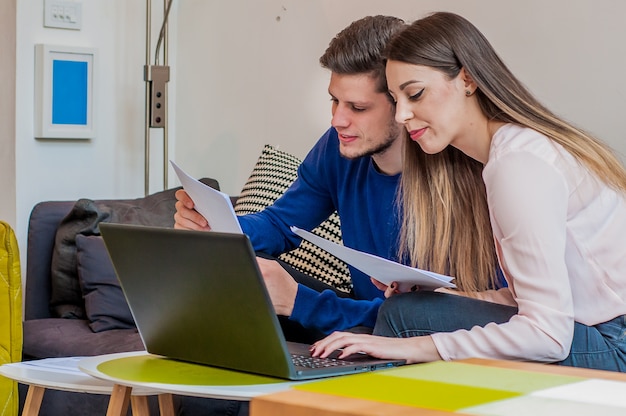 To iværksættere, der sidder sammen og arbejder ved et kontorbord og sammenligner dokumenter. Travlt par, der arbejder på kontoret og tæller finansielle data