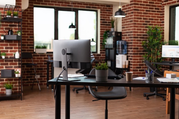 Tomt startup-kontor med computer og forsyninger på skrivebordet. Ingen i forretningsrum, der bruges til at arbejde på virksomhedens vækst med skærm og udstyr. Ingen mennesker på arbejdspladsen med dekorationer.