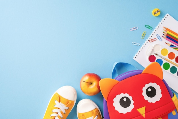 Top view of back to school essentials including shoes backpack apple and school supplies on blue background