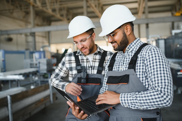 Two male international workers in overalls work together at a machine for the production of aluminum PVC windows and doors