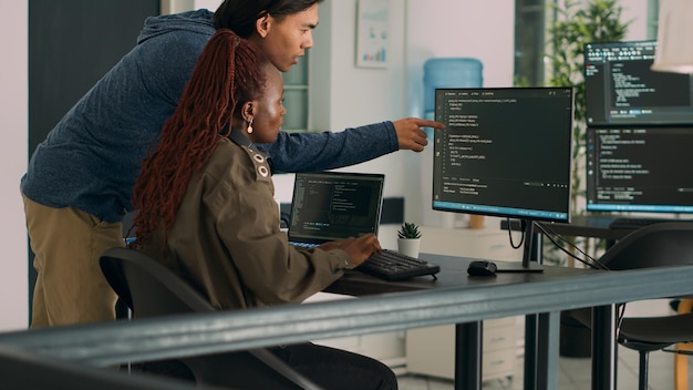 Two software coders analyzing source code on computer and laptop screen, using html script on terminal window. Team of system engineers working on cyber security innovation in it agency.