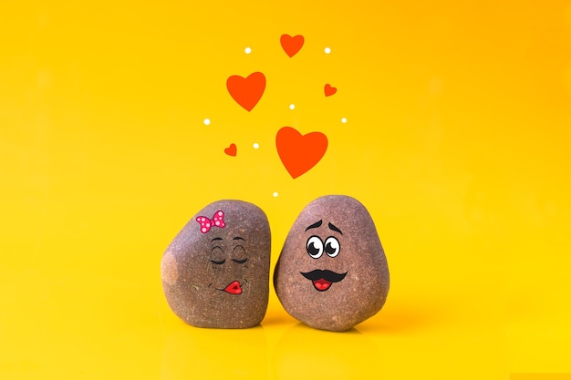 two stones with drawn funny faces in love with each other on yellow background. love, valentines day concept.
