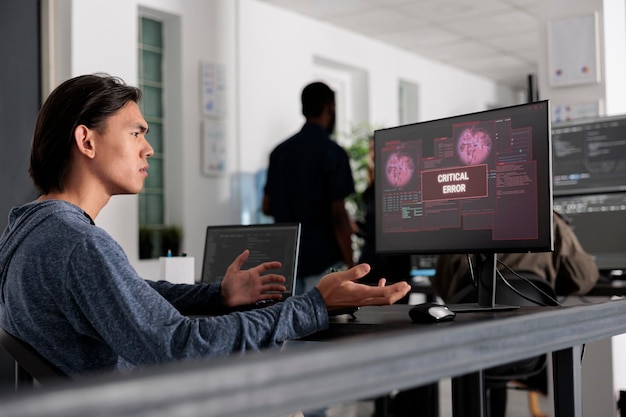 Web developer doing i don t know gesture while having web server hacked, looking at critical error on computer screen in it office. Engineer trying to solve hacking problem, firewall security.