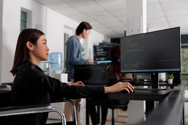 web developer in wheelchair working on server coding in big data office, analyzing programming language and script on terminal window. disabled woman programmer with impairment working on it system.