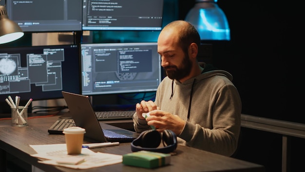 Web developer taking supplements out of box in office, using vitamins pills to work late at night. Programming cloud computing app code on terminal window, using medicine drugs.