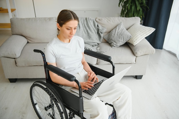 Woman in a wheelchair works on the laptop PC in the home office with an assistance dog as a companion