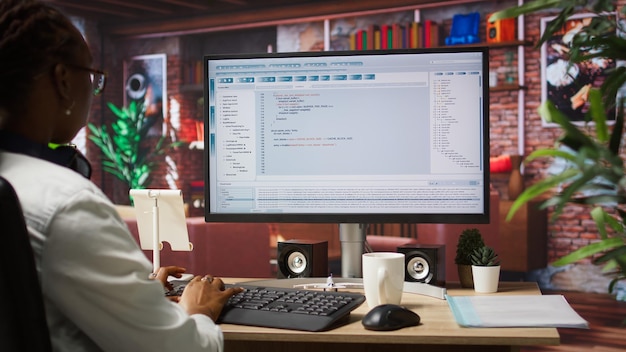 Woman in home office looking at UI on PC screen typing code