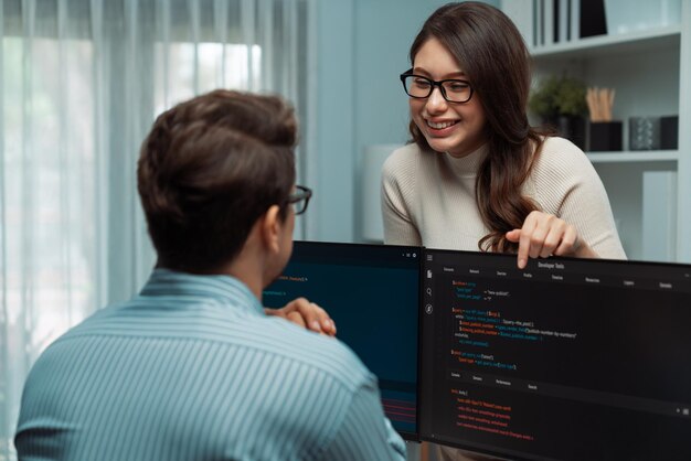 Woman standing opposite to man programmer working on desk to discuss postulate