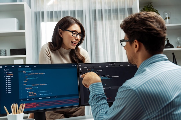 Woman standing opposite to man programmer working on desk to discuss postulate