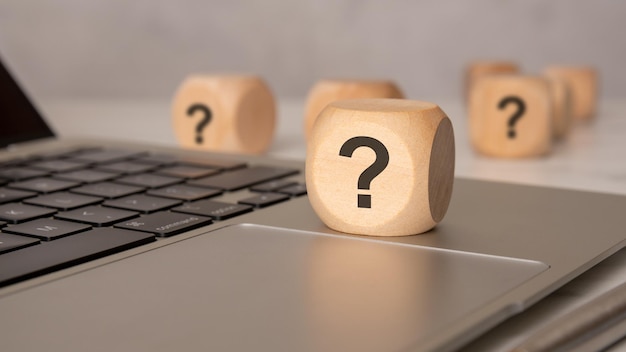 Wooden cube with question mark on laptop keyboard closeup concept image