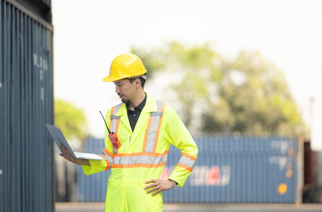 Workers in the import and export industry holding a laptop and standing on the front of container