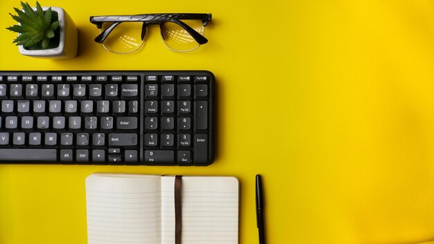 workspace desk with notebooks pens keyboard glasses plants and coffee on blue background