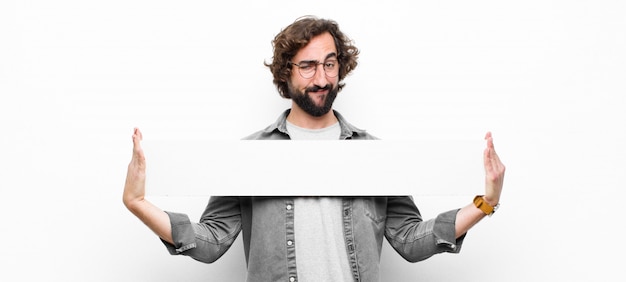 Young crazy cool man holding an empty placard or banner against white wall
