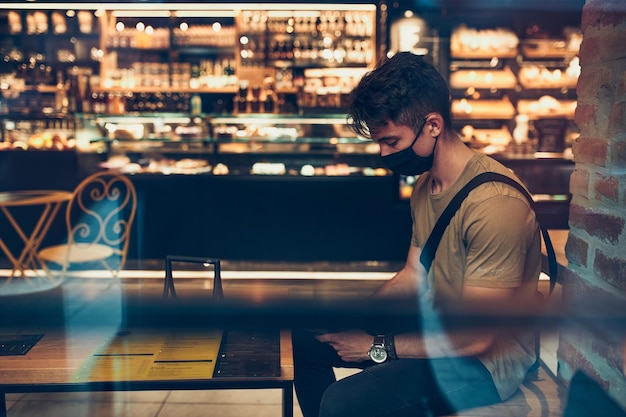 Young man sitting in coffee shop at store front in the city center in the evening