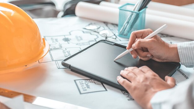 young man using tablet plotting a system of building structures in blueprints