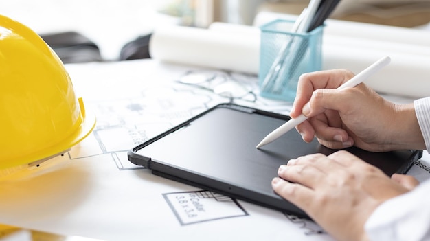 young man using tablet plotting a system of building structures in blueprints