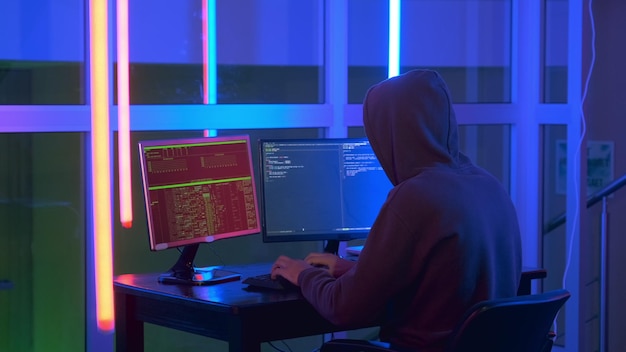 Young man wearing hood hacking by using computer and laptop at office