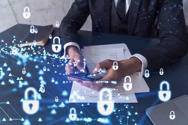 A businessman in formal wear reading the contract to prevent probability of risks in cyber security and checking details in the phone Padlock Hologram icons over the working desk