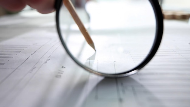 A person is holding a pencil and looking through a magnifying glass