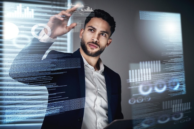 all the information is at my fingertips shot of a handsome young businessman standing alone in the office at night and using an interactive screen