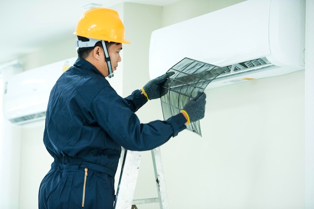 An Asian young Technician service man wearing blue uniform checkingProfessional air conditioner installer maintaining modern indoor air conditioner space for text