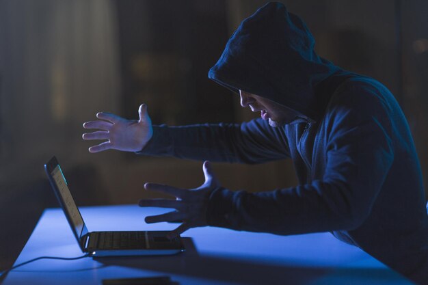 angry hacker with laptop computer in dark room