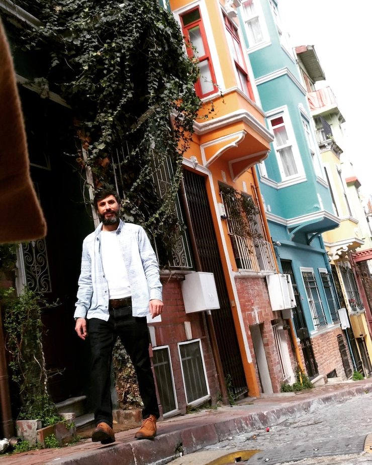 Fotoğraf binaya karşı patikada duran orta yaşlı adamın alçak açılı portresi