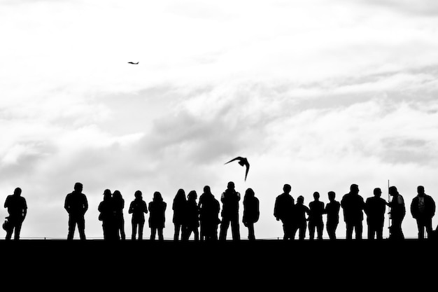 Bird flying over people standing on footbridge against cloudy sky
