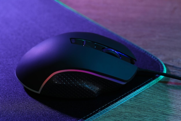 Black computer mouse and mousepad on wooden table in neon lights closeup