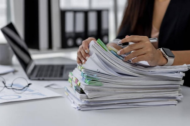 Businesswoman hands working in Stacks of paper files for searching and checking unfinished document achieves on folders papers at busy work desk office