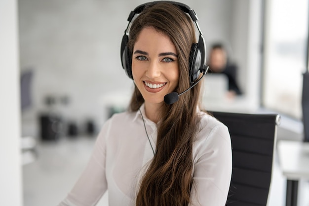 Close up portrait of service desk consultant woman talking using handsfree headphones with microphone Smiling beautiful woman working as call center agent with headset in bright modern office