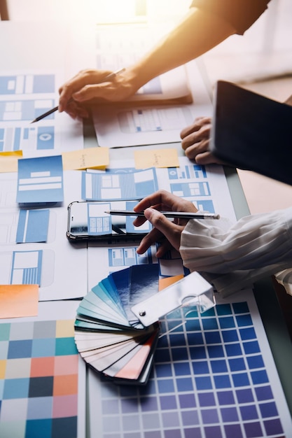 Close up ux developer and ui designer brainstorming about mobile app interface wireframe design on table with customer breif and color code at modern officeCreative digital development agency