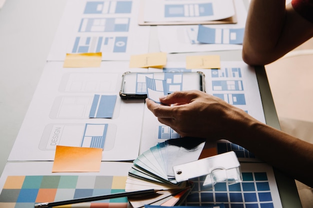 Close up ux developer and ui designer brainstorming about mobile app interface wireframe design on table with customer breif and color code at modern officeCreative digital development agency