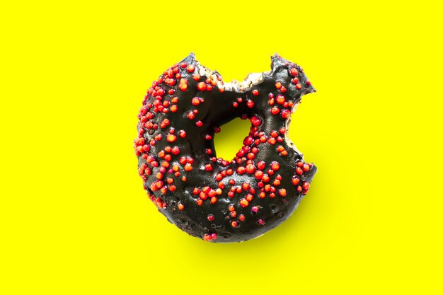 Creative concept of biting eating delicious sweet sugar black doughnut donut with red glaze bited on yellow background Top view flat lay unhealthy dessert Food concept