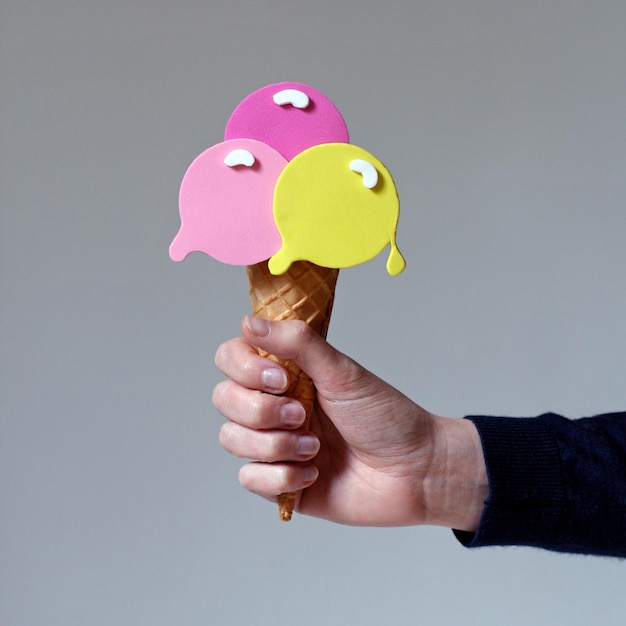 cropped hand holding artificial ice cream against gray background