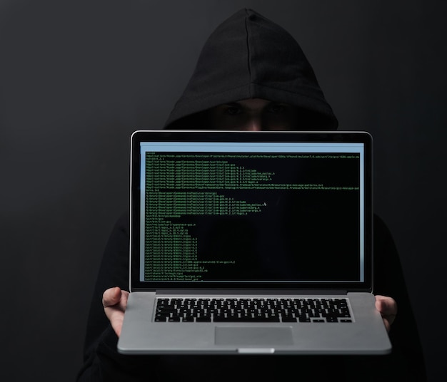 Dark hoodie and hacker in studio laptop and fraud of cybersecurity online and hiding with screen Black background scam and coding of criminal programming and ransomware with error and person