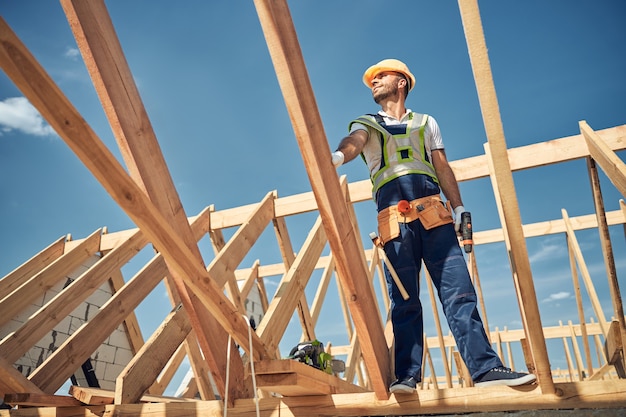 Delighted male person standing high on the frame for future roof