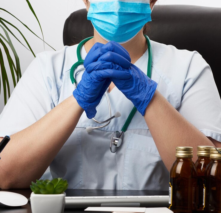 Fotoğraf doctor in a white coat and blue latex gloves sits at a white work table in his office conc