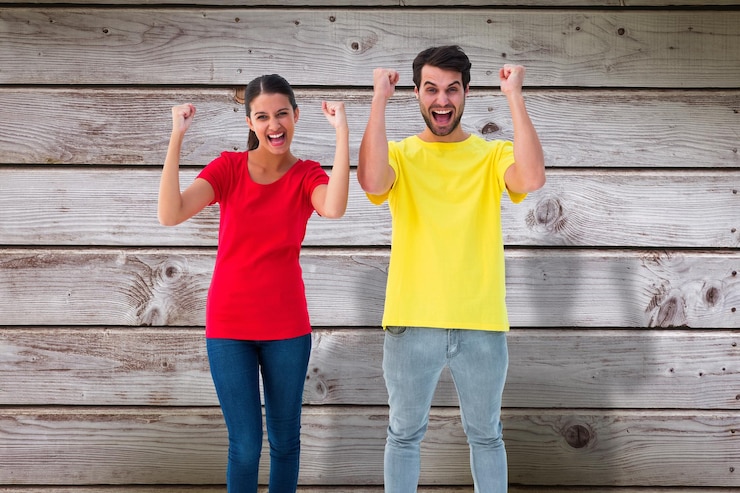 Fotoğraf excited couple cheering in red and yellow tshirts against digitally generated grey wooden planks