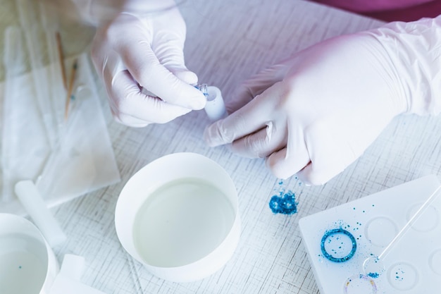 Female hands in gloves pour sparkles into a mold for making a pendant from epoxy resin