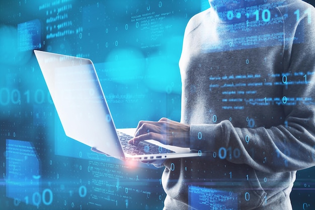 hacker in hoodie using laptop computer with abstract glowing blue coding background binary code theft technology data and internet concept double exposure