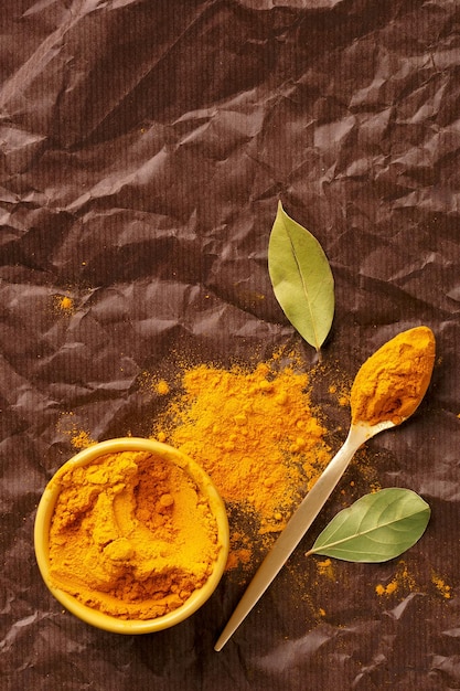 High angle view of curry powder in bowl with bay leaves on paper