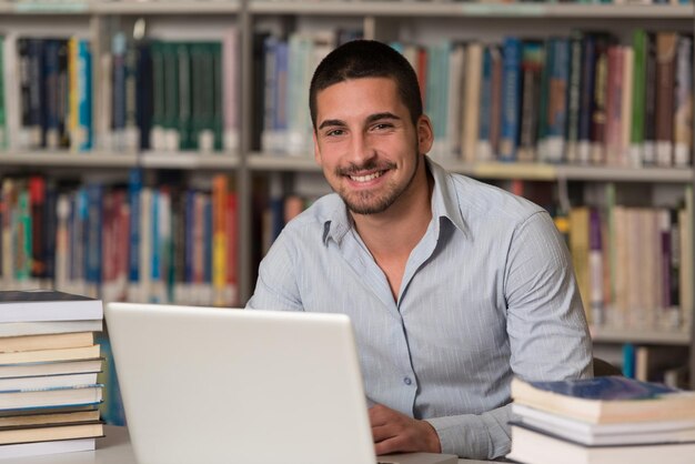 In The Library  Handsome Male Student With Laptop And Books Working In A High School  University Library  Shallow Depth Of Field