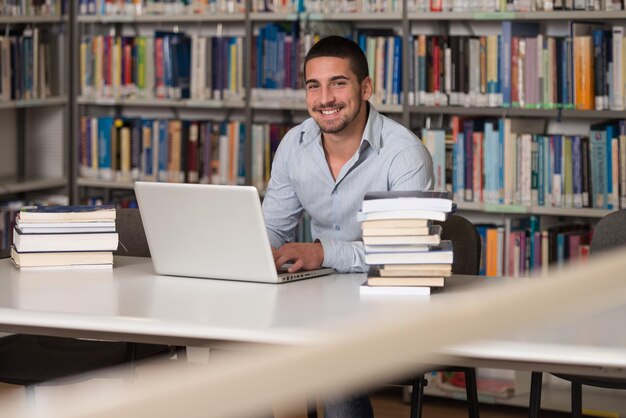 In The Library  Handsome Male Student With Laptop And Books Working In A High School  University Library  Shallow Depth Of Field